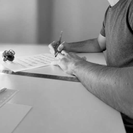 A writer resting the forearms lightly on the table while practising with an oblique penholder.