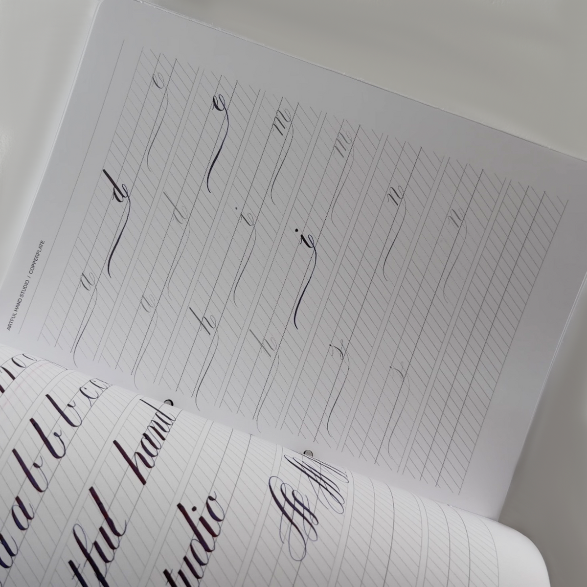 Open Copperplate calligraphy workbook showing lowercase letter practice and ruled guidelines.